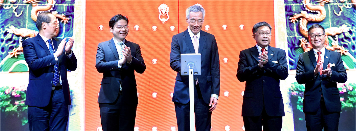 Five men in suits clapping against a backdrop with ornate designs. Lee Hsien Loong is centered.